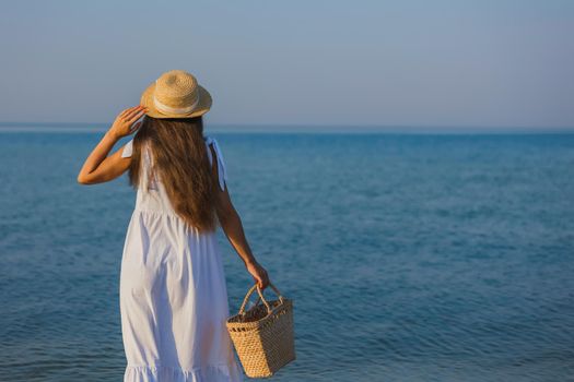 woman in a hat and with a basket in her hands is walking on the beach