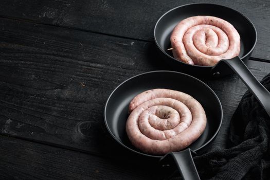 Raw spiral sausage set in cast iron frying pan, on black wooden table background , with space for text copyspace