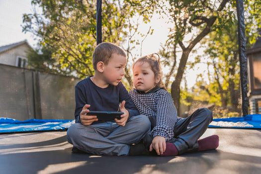 children sit on a trampoline and look at the phone