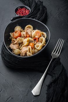 Whole wheat pasta with dried tomatoes and tuna in bowl, on black background