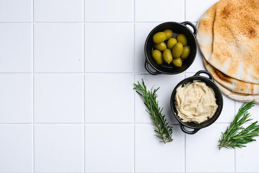 Hummus and pita bread, on white ceramic squared tile table background, top view flat lay, with copy space for text