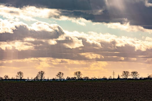 A field, trees, windmills and a spectacular sky with dramatic dark and reddish clouds and sunbeams