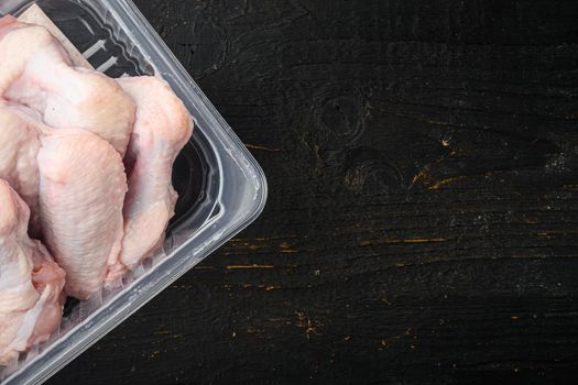 Raw chicken wings in plastic pack set, on black wooden table background, top view flat lay, with copy space for text