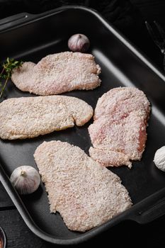 Homemade raw breaded German Weiner Schnitzel, on black wooden table background