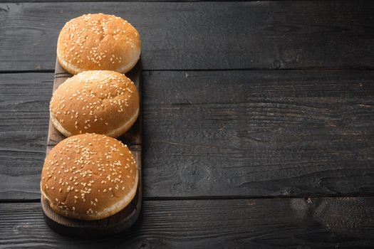 Fresh homemade burger buns with sesame set, on wooden serving board, on black wooden table background, with copy space for text
