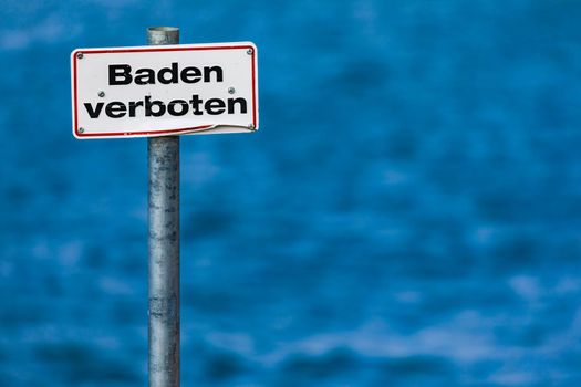 German sign prohibiting bathing with a red border in front of a standing body of water in Germany