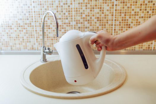 kettle in a hand pouring fresh purified water under a filter tap