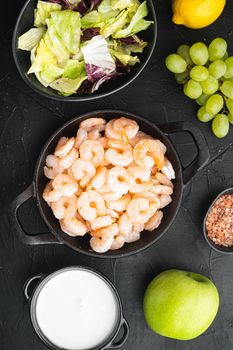 Fresh summer vitamin appetizer of green salad, shrimps, olive ingredients set, with sauce apple and grape, on black stone background, top view flat lay