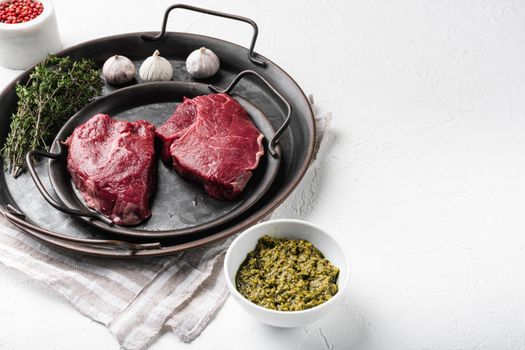 Raw beef meat steak with herbs set, on white stone table background, with copy space for text