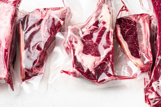 Raw beef meat in the vacuumed skin pack set, tomahawk, t bone, club steak, rib eye and tenderloin cuts, on white stone background