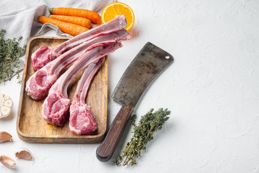 Raw Lamb Filets on bone set, with ingredients carrot orange, herbs, and old butcher cleaver knife, on white stone background , with copyspace and space for text