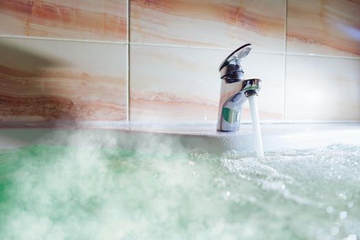 water tap pouring hot water in a bath tub with steam