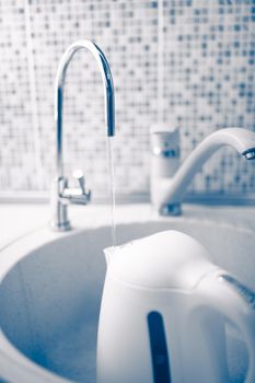 kettle pouring with fresh purified water under a filter tap