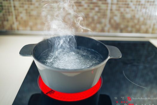 white boiling pot with hot steam on electrical induction cooktop