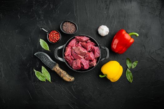 Beef stew prepared for goulash cooking set with sweet bell pepper, in cast iron frying pan, on black stone background, top view flat lay, with copy space for text