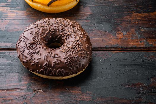 Breakfast chocolate donuts, on old dark wooden table background with copy space for text