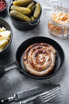 Fried Bavarian German Nürnberger sausages with sauerkraut, mashed potatoe in cast iron frying pan, on gray background