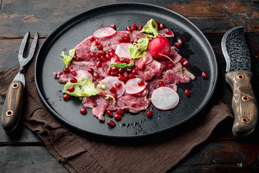 Carpaccio of marbled beef set, with Radish and garnet, on plate, on old dark wooden table background