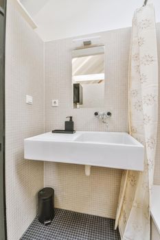 Cupboard with sink and mirror attached to tiled wall near door and drying rack in modern restroom