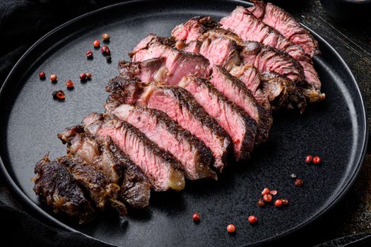 Sliced grilled rib eye beef steak beef marbled rare set, on plate, on old dark rustic background