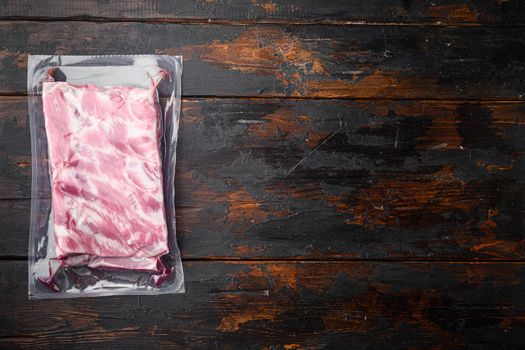 Pork ribs in a vacuum bag set, on old dark wooden table background, top view flat lay, with copy space for text