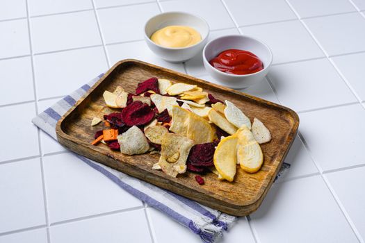 Dried vegetables chips from carrot, beet, parsnip and other vegetables set, on white ceramic squared tile table background, with copy space for text
