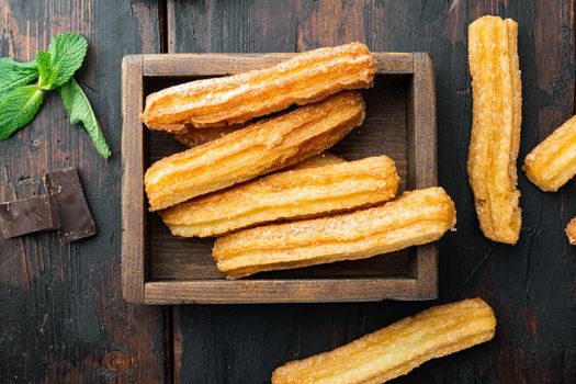 Traditional churros sticks with cinnamon and sugar powder set, on old dark wooden table background, top view flat lay