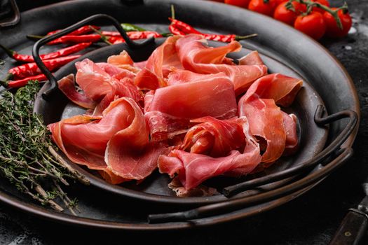 Delicious Spanish jamon or ham, on black dark stone table background