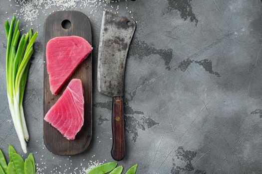 Raw tuna steak, fresh red tuna fillet with ingredients, green pea, sesame and spices set, on wooden cutting board, and old butcher cleaver knife, on gray stone background, top view flat lay , with copyspace and space for text