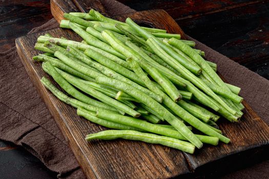 Fresh green French beans set, on wooden cutting board, on old dark wooden table background