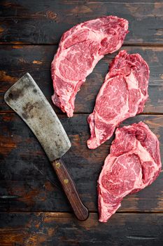 Raw ribeye steak marbled meat with salt, rosemary and garlic set, and old butcher cleaver knife, on old dark wooden table background, top view flat lay