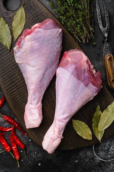 Raw turkey drumsticks with thyme, pepper set, on black dark stone table background, top view flat lay