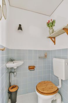 Modern flush toilet and ceramic sink mounted on blue tiled walls in a small lavatory at home with wood elements