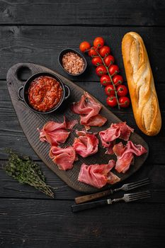 Italian prosciutto crudo or spanish jamon, on black wooden background, top view flat lay