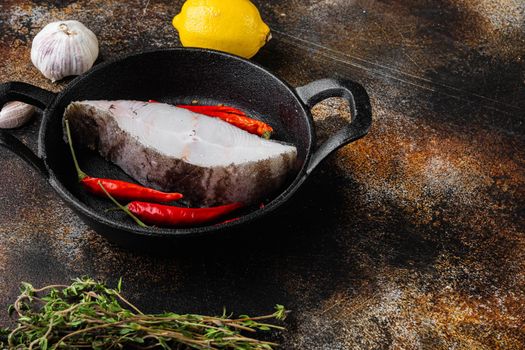 Raw steak of white fish set, with ingredients and rosemary herbs, on old dark rustic table background, with copy space for text