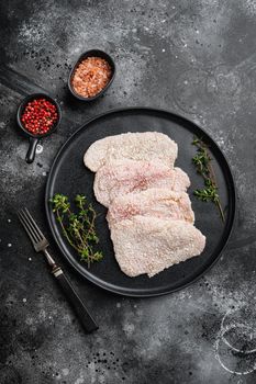 Raw schnitzel chicken meat, on black dark stone table background, top view flat lay, with copy space for text