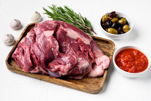Raw lamb shoulder meat ready for baking set, with ingredients and herbs, on white stone table background, with copy space for text