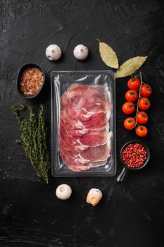 Cured ham jamon vacuum plastic pack set, on black dark stone table background, top view flat lay, with copy space for text