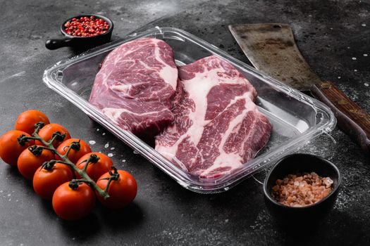Beef steak in vacuum packing. Market Chuck Eye Roll set, on black dark stone table background