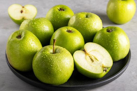 Fresh ripe green apples on a black ceramic plate on a gray background. Harvest, healthy food concept. Selective focus.