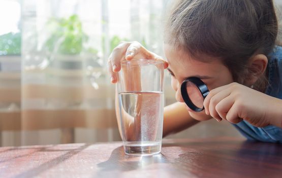 The child examines the water with a magnifying glass in a glass. Selective focus. Kid.