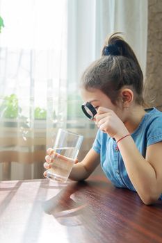 The child examines the water with a magnifying glass in a glass. Selective focus. Kid.