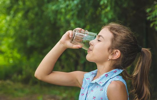 Child girl drinks water from a glass. Selective focus. Kid.