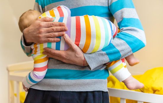 The father puts the baby to sleep in his arms. Selective focus. People.
