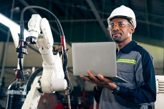African American factory worker working with adept robotic arm in a workshop . Industry robot programming software for automated manufacturing technology .
