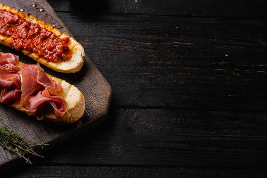 Traditional Spanish Jamon Serrano ham set, on black wooden table background, with copy space for text