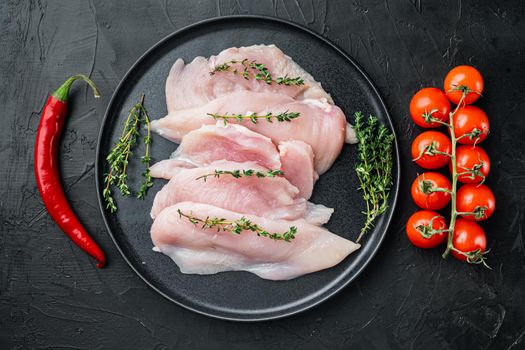 Pieces of raw and uncooked chicken fillets, on black background, top view flat lay