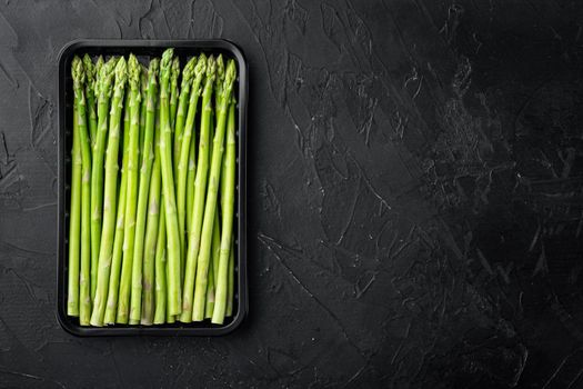 Fresh of green Asparagus. Cooking healthy meal. Bunches of green asparagus set, in plastic market container, on black stone background, top view flat lay, with copy space for text