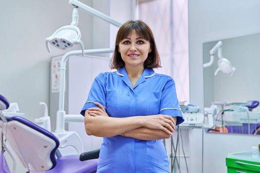 Portrait of smiling nurse looking at camera in dentistry. Confident female with folded hands, dental clinic equipment background. Dentistry, medicine, health care, profession, stomatology concept