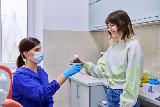 Dentist doctor showing telling giving medicine for teeth and oral cavity in bottle to young teenage female in office. Dentistry, health care, treatment, people, medicine concept